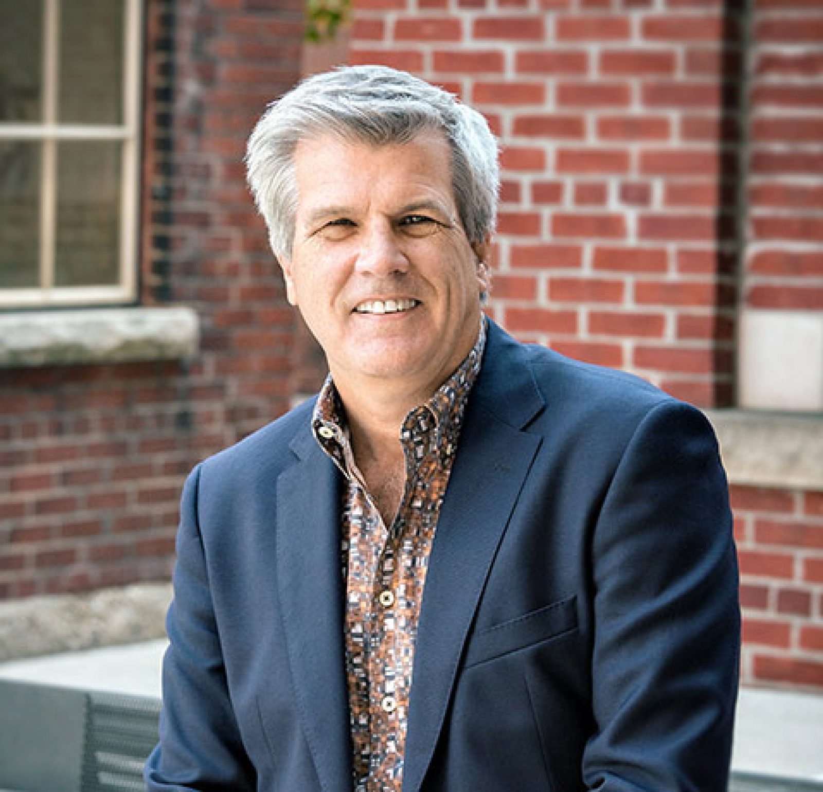 Headshot of former FORREC CEO Gord Dorrett with short blonde hair, in a dark blazer with a brick wall background