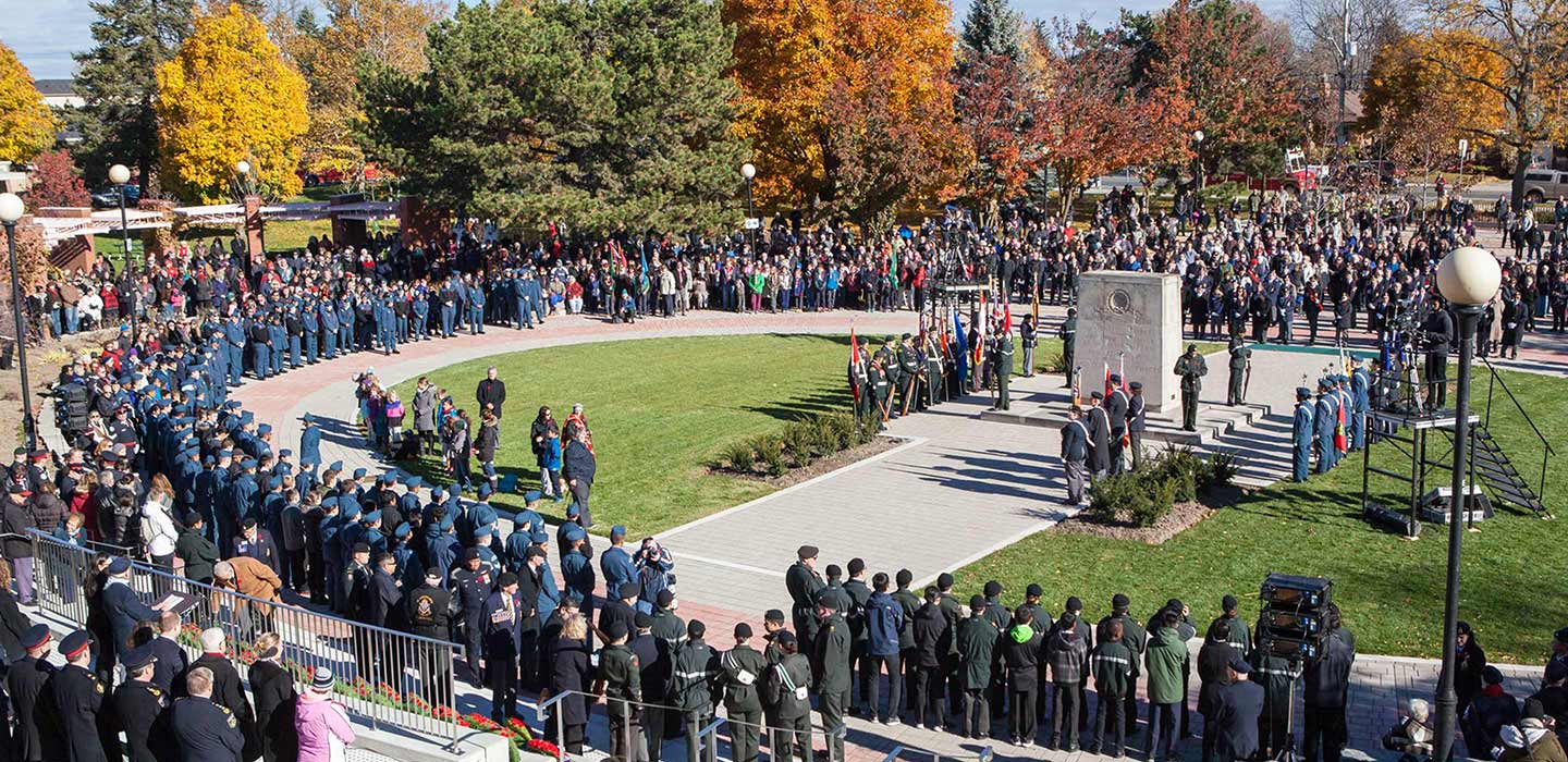 Large gathering of people at the downsview memorial parkette cadets in blue uniform stand with flags at rectangle statue