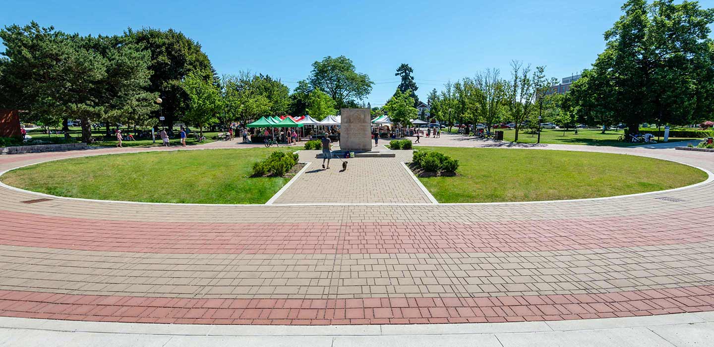 View from entrance of East york civic centre of greenery and tents behind statue surrounded by red and grey brick road