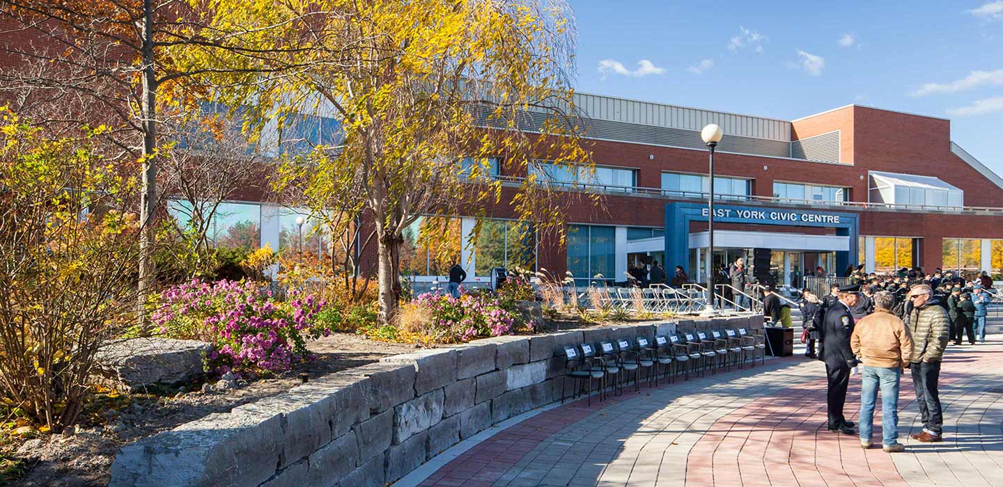 Entrance doors to east york civic centre with blue sign and people gathered in front