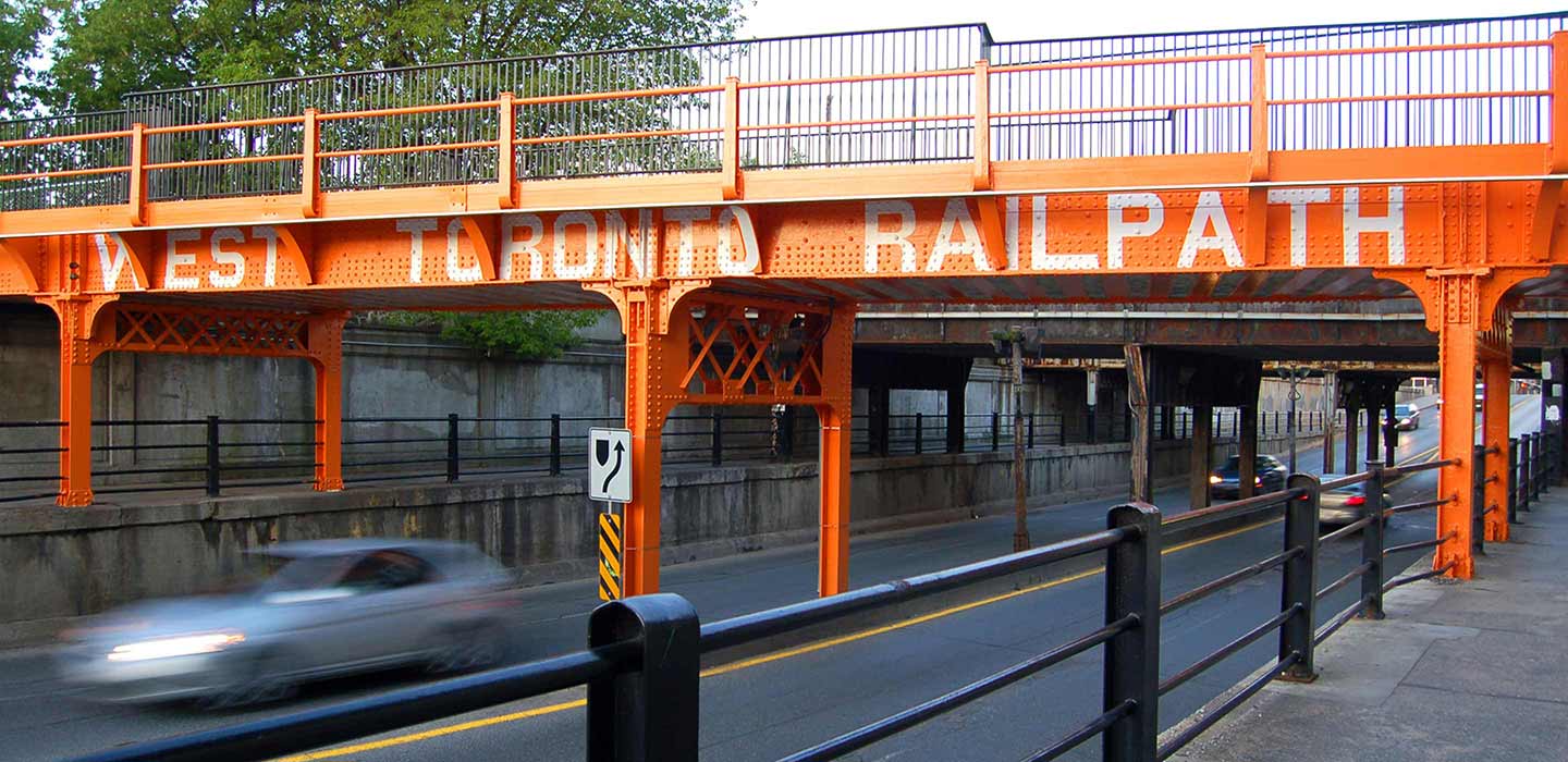 orange bridge over city streets with copy West Toronto Railpath in white