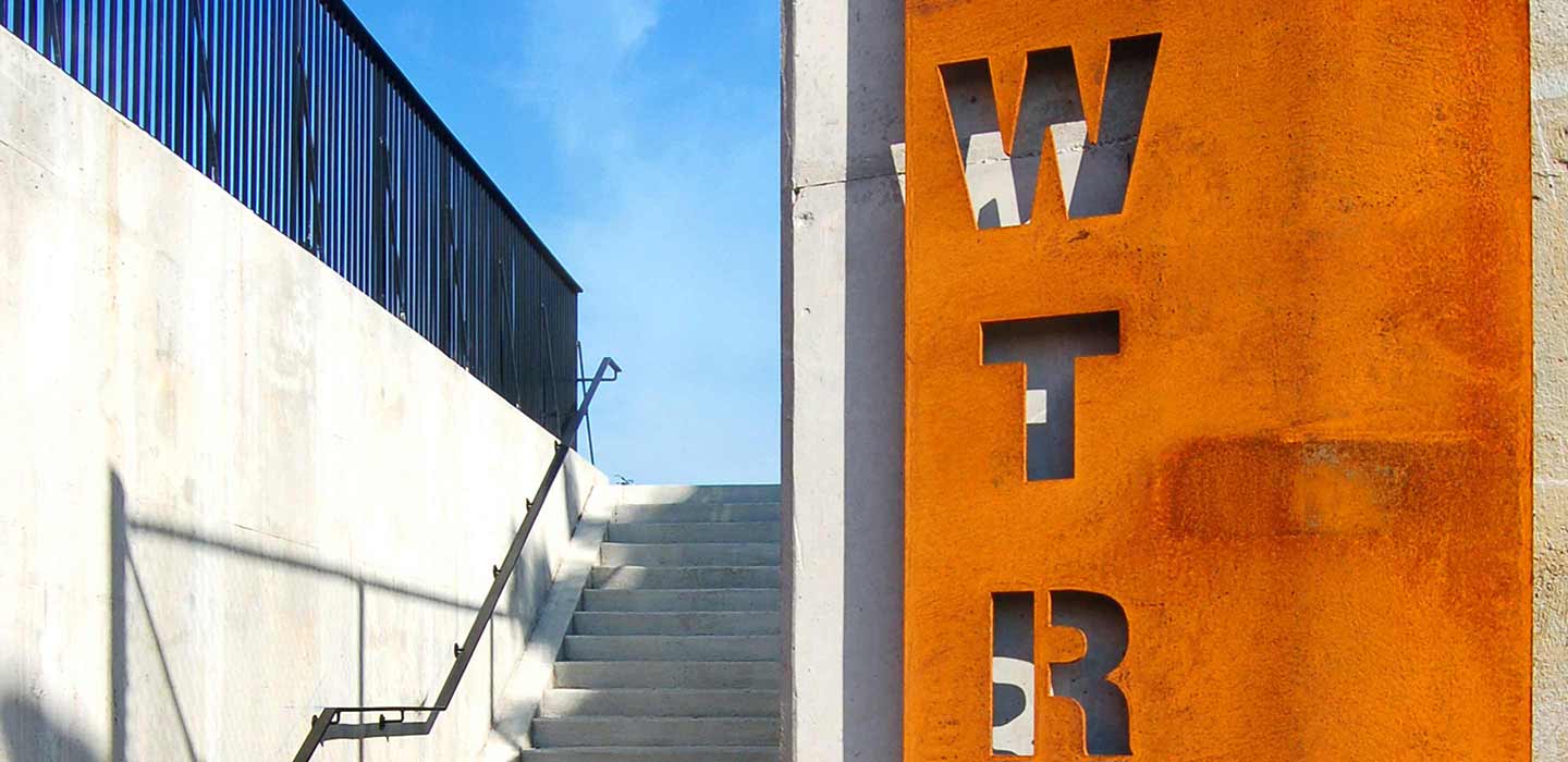 Orange West Toronto Railpath sign with cut out letters W T R next to concrete staircase outside