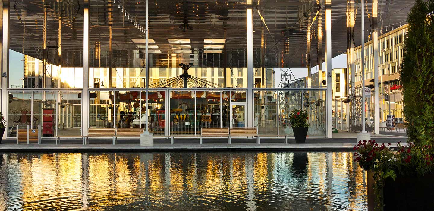 big glass windows on the water looking into covered area with merry go round ride inside at downsview parkette