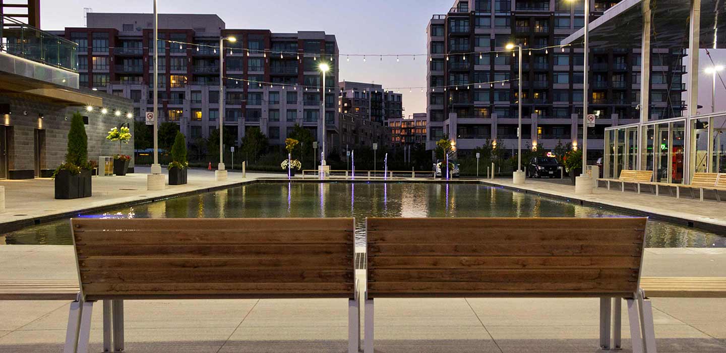 Two wooden benches in front of grey pool full of water at downsview memorial parkette