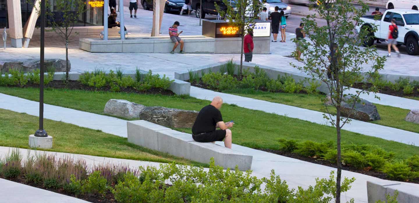 Man sitting on concrete bench outside of Tronto Public Library surrounded by green grass
