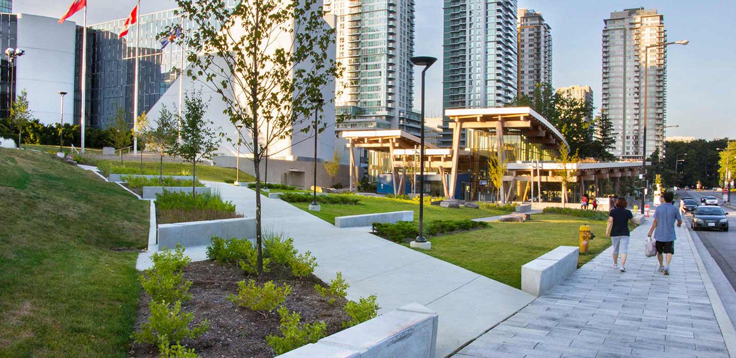 picture of concrete walkway surrounded by green grass and tress with city skyscrapers in the background