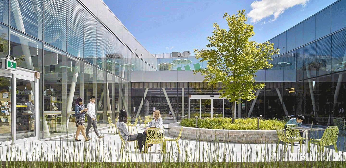 Vaughn Civic Centre outdoor courtyard surroudned by wglass buidling with people sitting at green and grey tables and a big green try in the centre