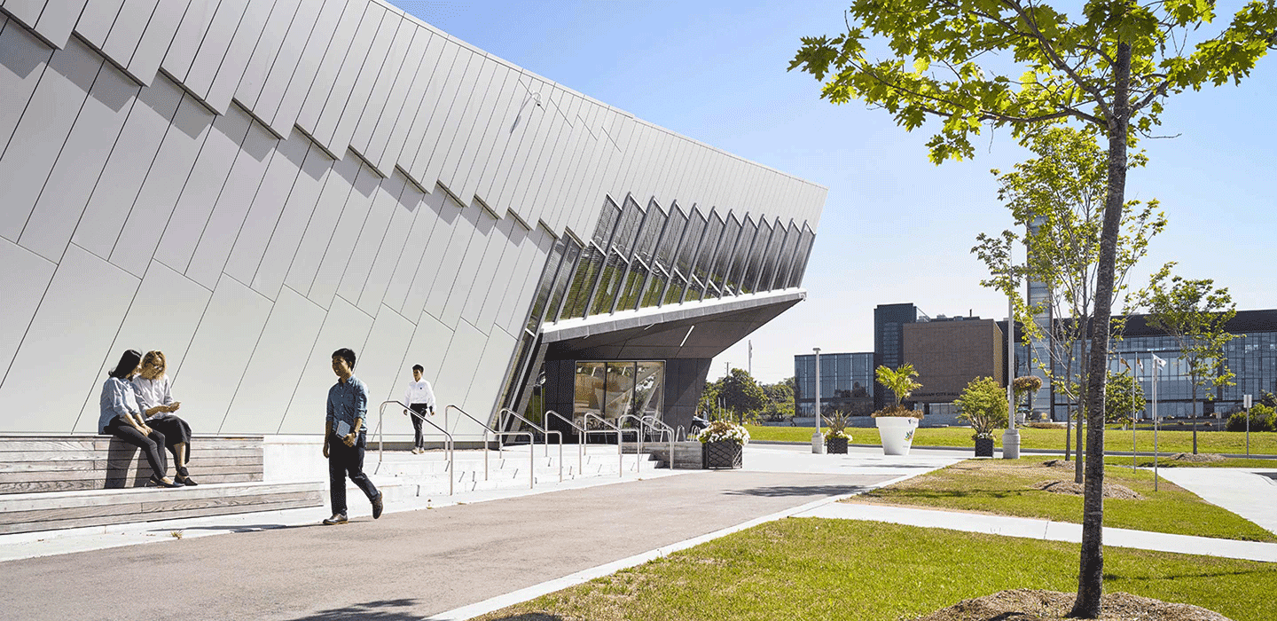 Outside of Vaughn Civic Centre showing white and grey buidling with diagonal panel and window desig, greenery surrounding and people walking