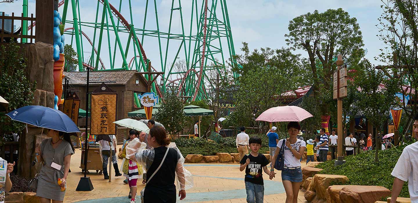 People walking around Wanda Nanchang Theme Park with green rollercoaster in the background