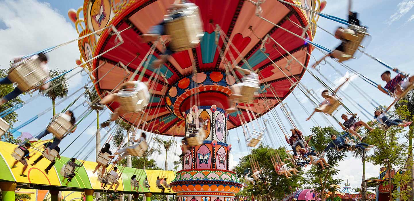 Red, pink and blue merry go round spinning with people sitting in the swings at Wanda Xishuangbanna Theme Park