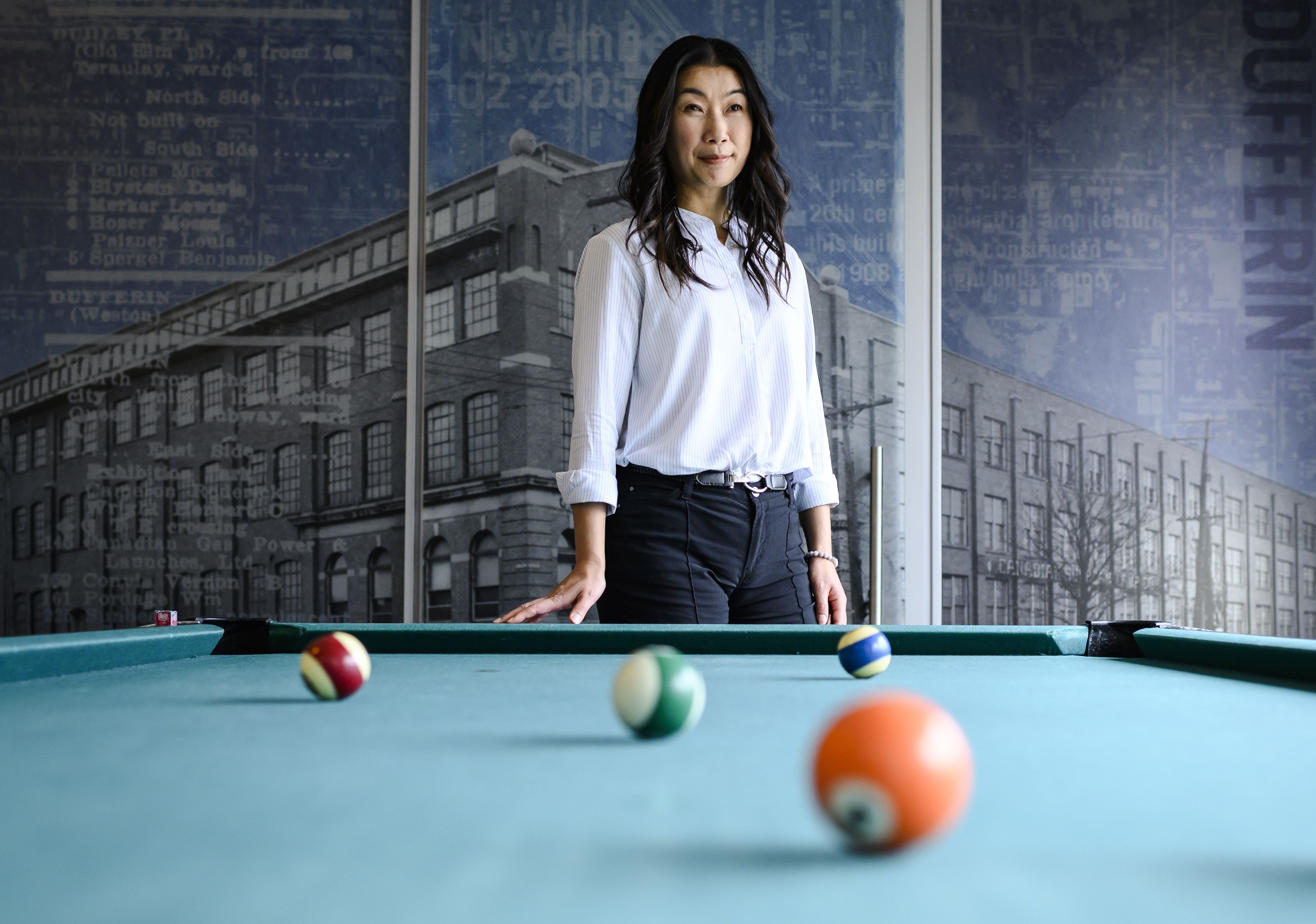 Linda Hung standing behind pool table with a photo of a brick building in background